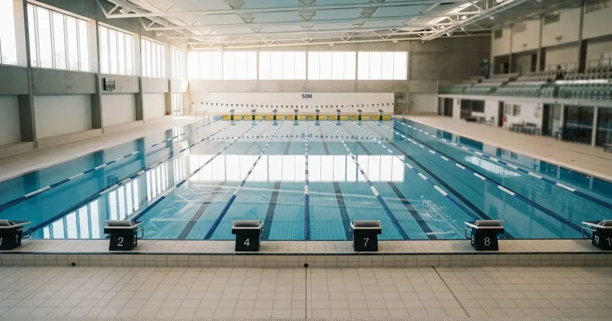 Pusty basen olimpijski z równymi torami i spokojną taflą wody, widok z trybun w jasnym świetle.